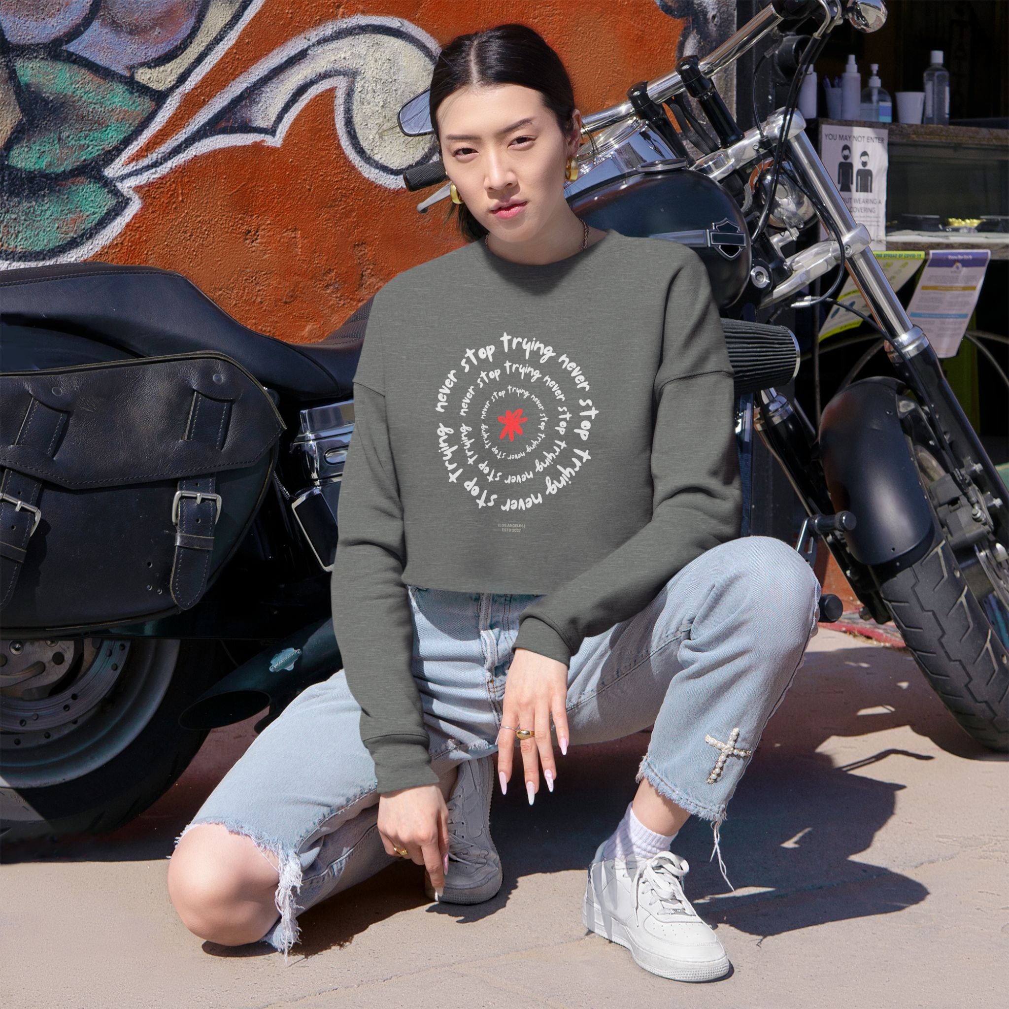 Person wearing a gray sweatshirt with text and graphics, sitting in front of a motorcycle.