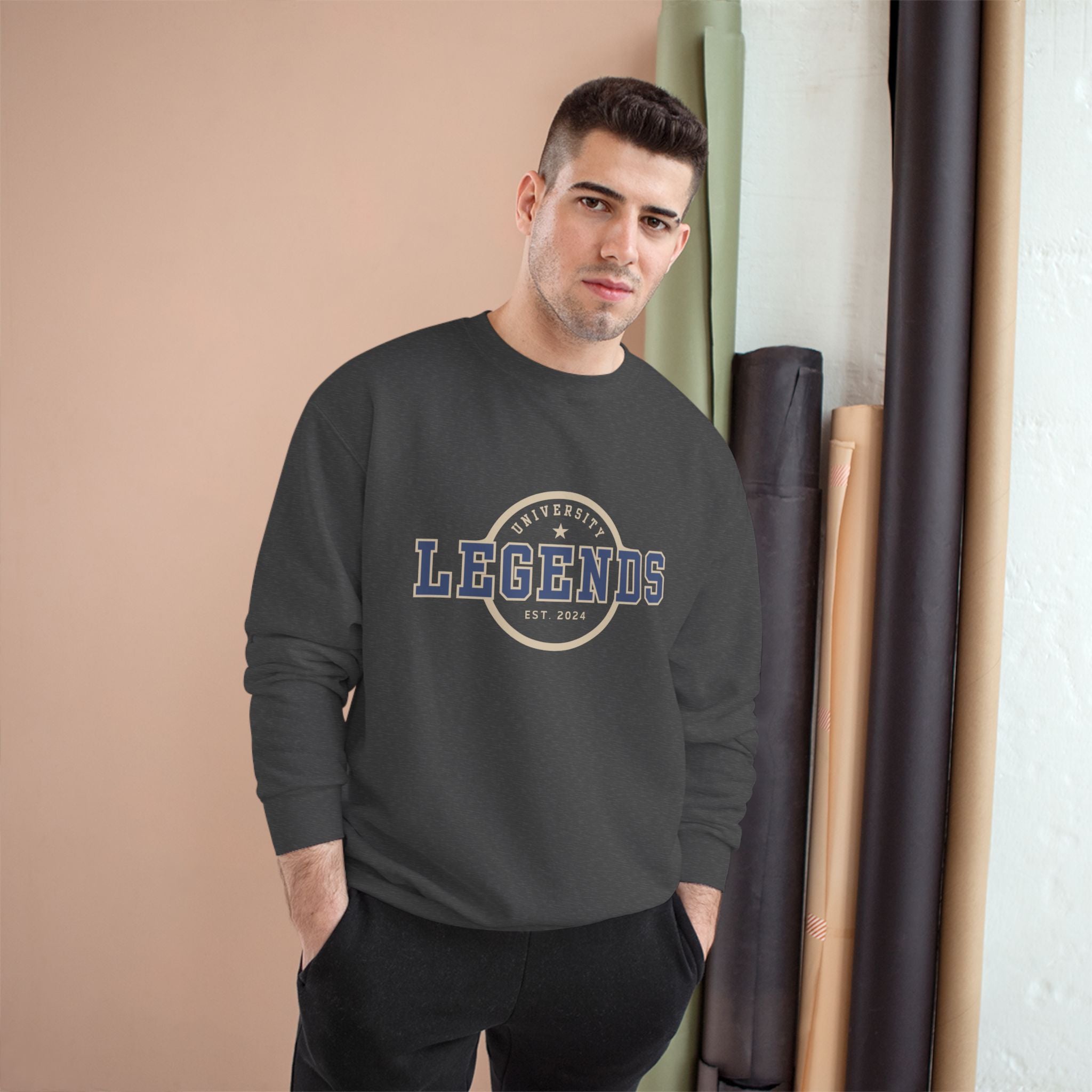 Man wearing a dark gray sweatshirt with 'Legends' print, standing indoors against a beige wall.