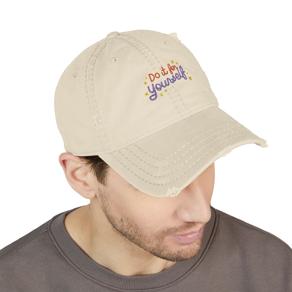 Beige cap with 'Do it Yourself' text worn by a person on a white background