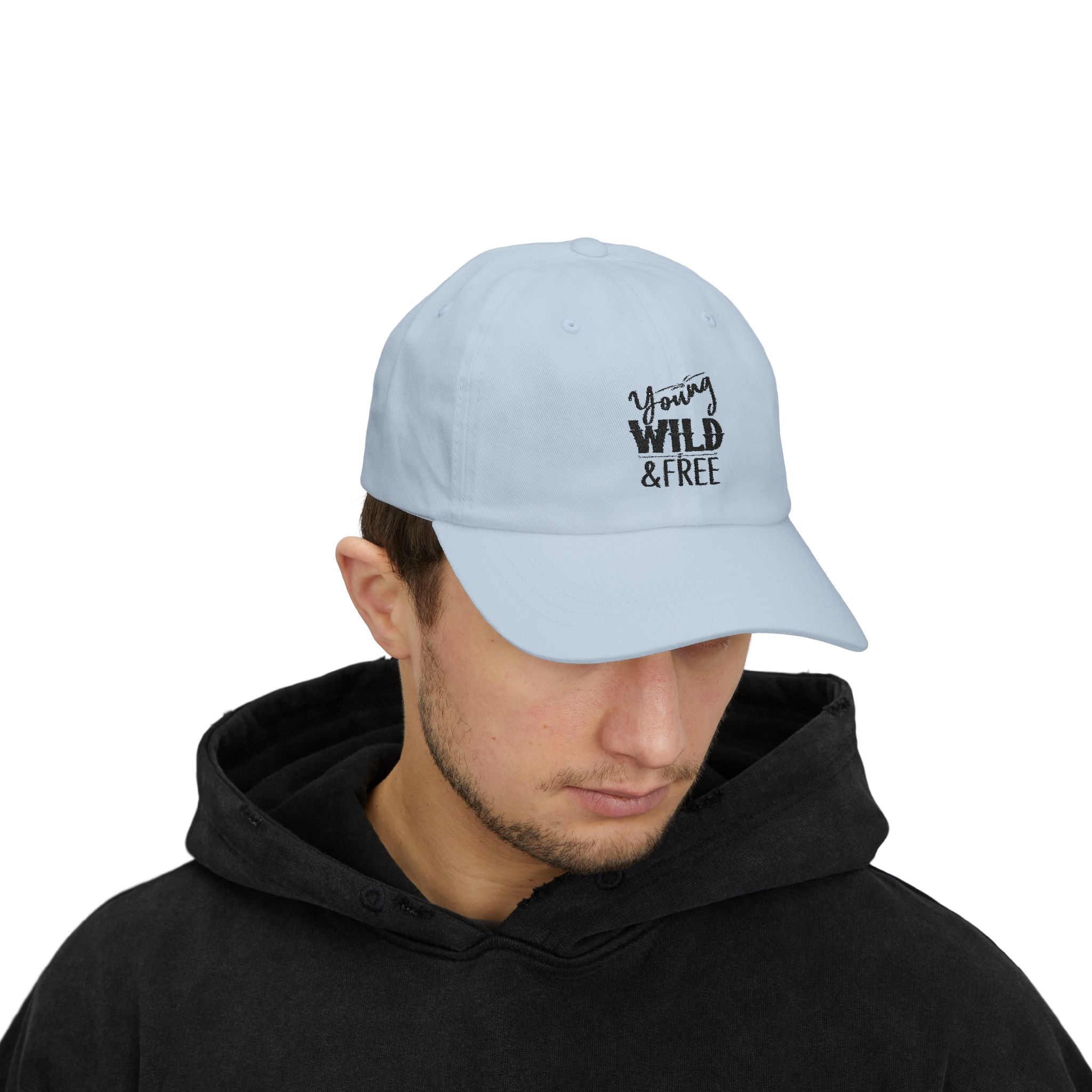 Light blue cap with 'Young Wild Free' text worn by a person in a black hoodie on a white background