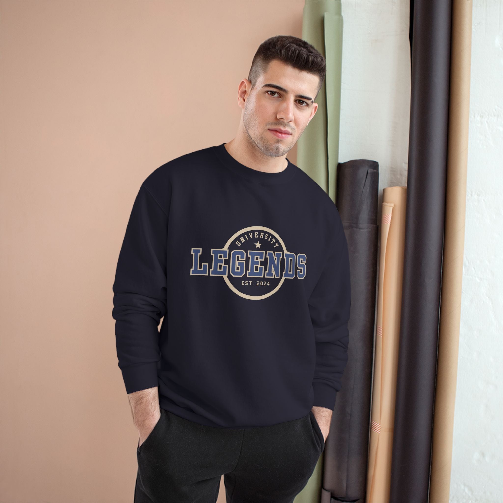 Man wearing a navy blue sweatshirt with 'Legends' print, standing indoors against a beige wall.