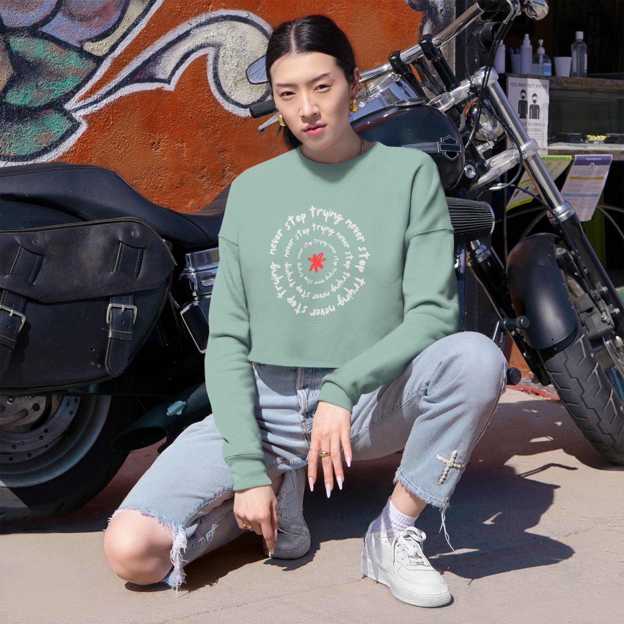 Person wearing a green sweatshirt with text and graphics, sitting in front of a motorcycle.