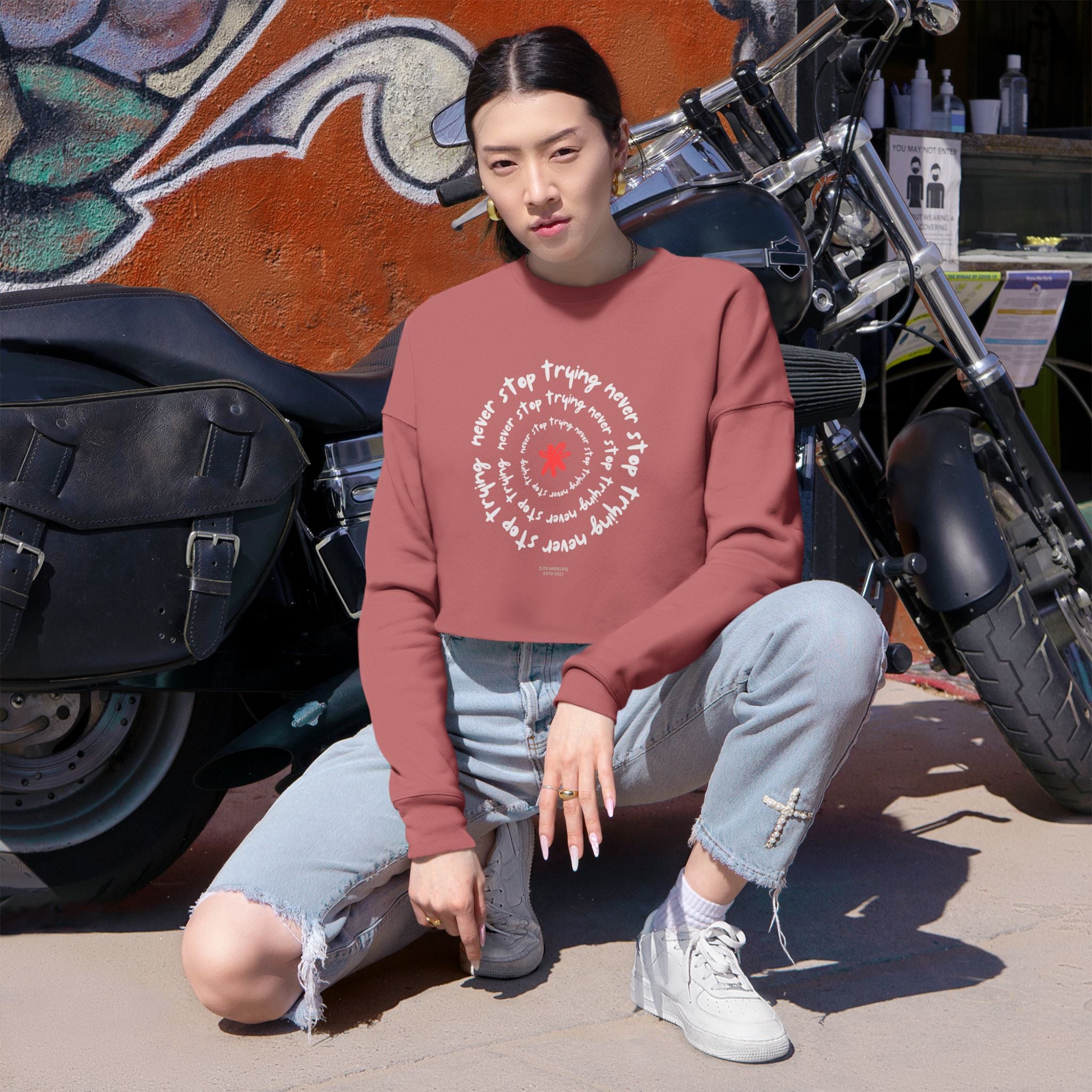Person wearing a maroon sweatshirt with text and graphics, sitting in front of a motorcycle.